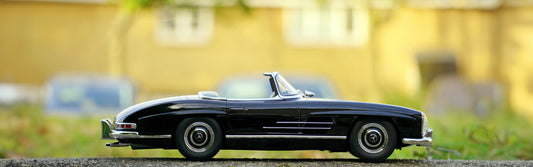 A highly detailed diecast model of a black classic convertible car, displayed outdoors with a blurred background, highlighting the car's sleek design and intricate features.